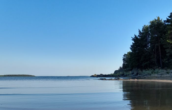 Kuva rannalta ulapalle päin. Horisontissa näkyy saari. Vesi on tyyni.