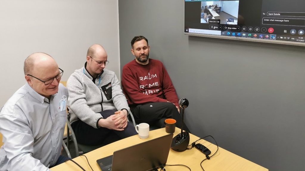 Kolme henkilöä MerSol-hankkeen palaverissa, pöydällä tietokone ja ruudulla osallistujia etäyhteydellä.