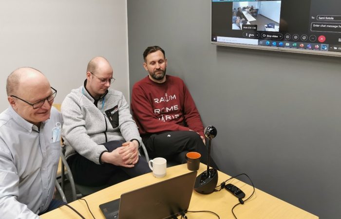 Kolme henkilöä MerSol-hankkeen palaverissa, pöydällä tietokone ja ruudulla osallistujia etäyhteydellä.