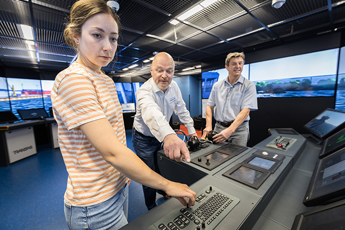 Kolme henkilöä ohjaa merenkulun simulaattoria.