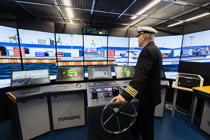 Kapteenin virka-asussa oleva henkilö ohjaa merenkulun simulaattoria.