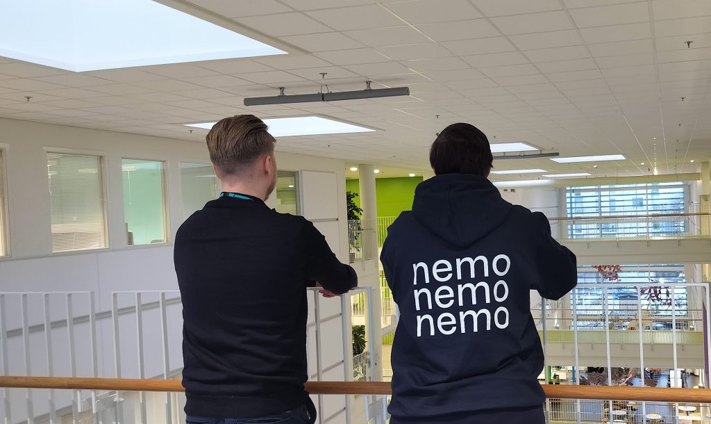 Kaksi henkilöä seisomassa selät kameraan päin. Toisella Nemo-projektin huppari päällä.