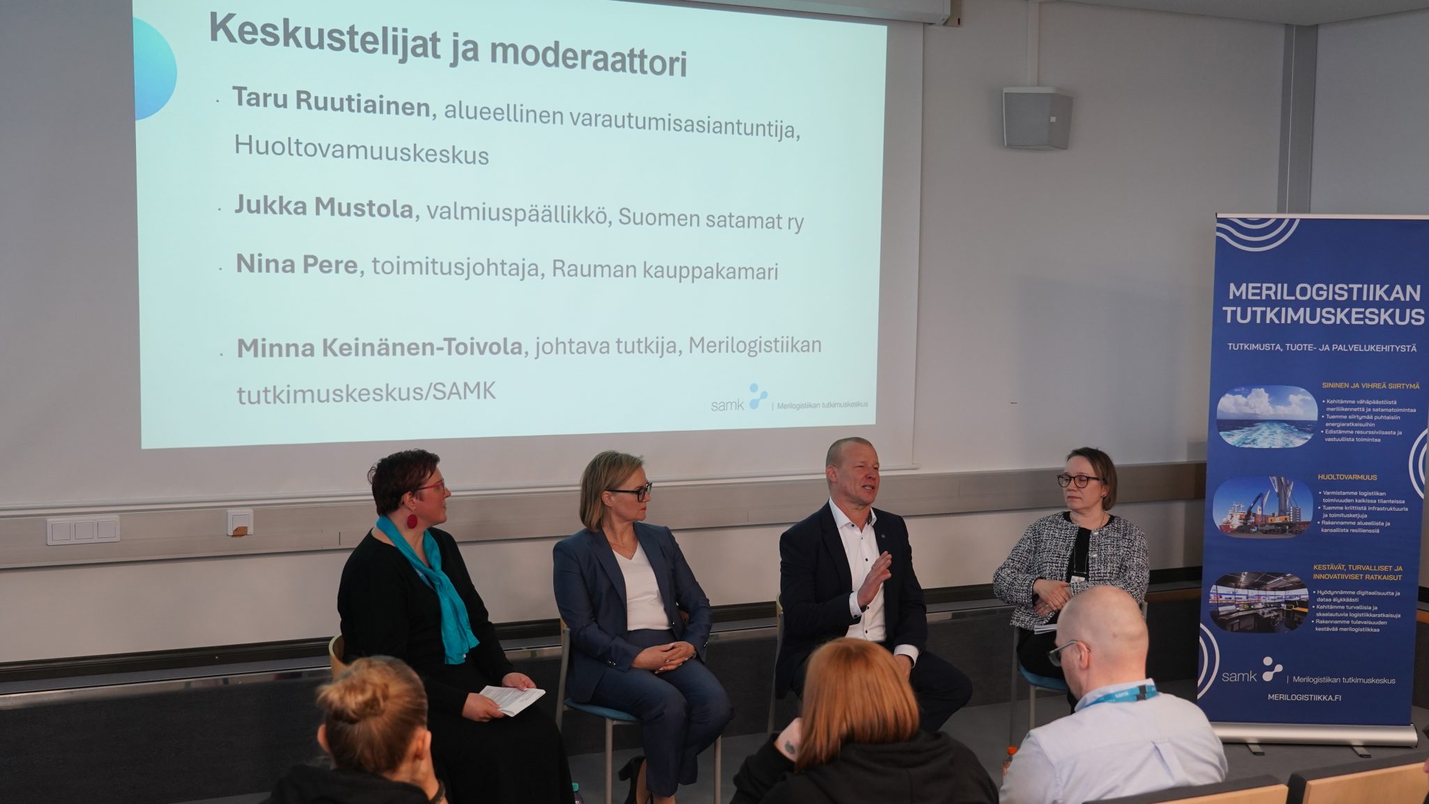 teemakeskustelun osallistujat istumassa auditorion edessä esiintymispaikalla.