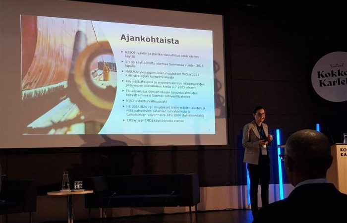 Henkilö esittämässä tapahtuman aikataulua. Taustalla diaesitys.