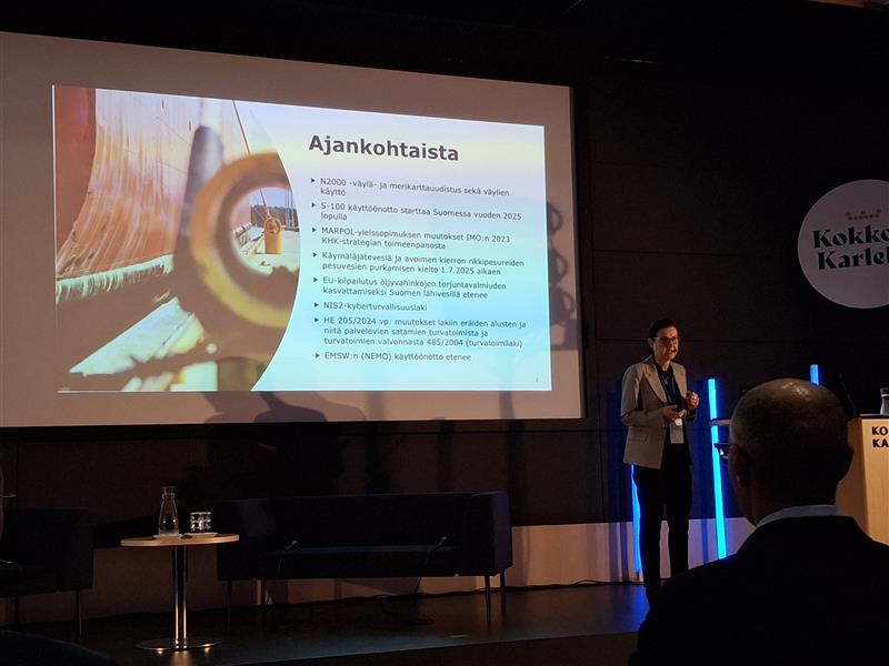 Henkilö esittämässä tapahtuman aikataulua. Taustalla diaesitys.