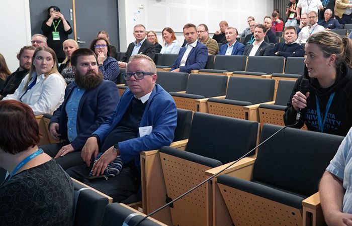 Tutkimusfoorumin yleisöä auditoriossa. Yleisöstä yksi henkilö puhuu mikrofoniin.