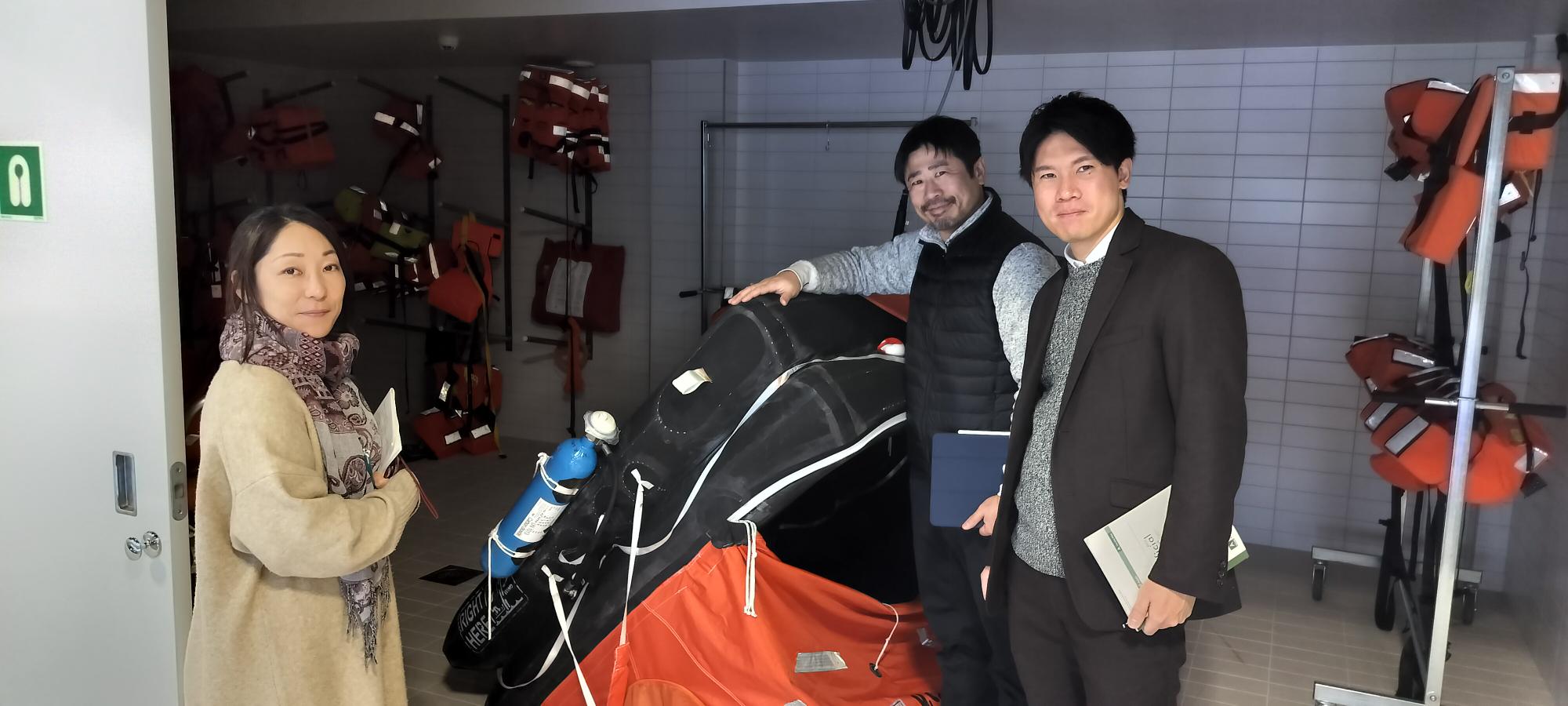 Koki Matsushima, Shohei Goto, and Asami Shimada pose next to maritime rescue equipment in a classroom.