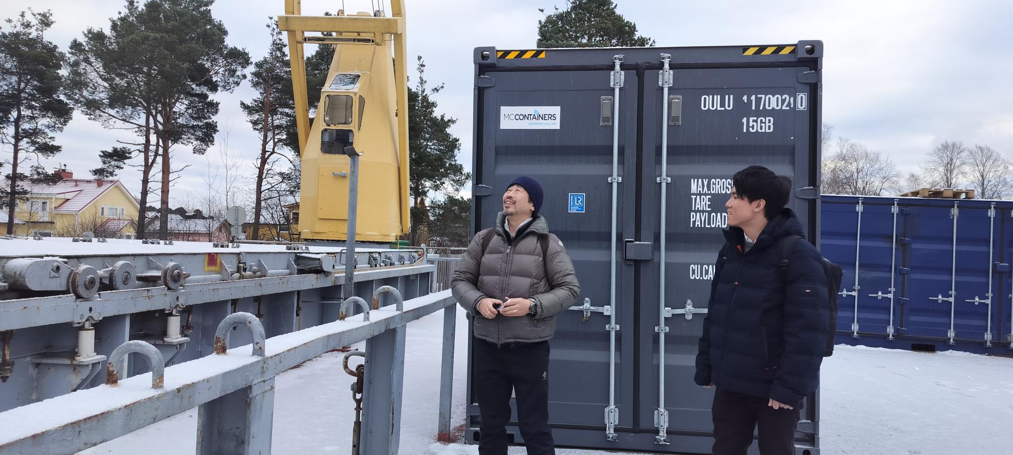 Koki Matsushima and Shohei Goto stand in front of a shipping container.