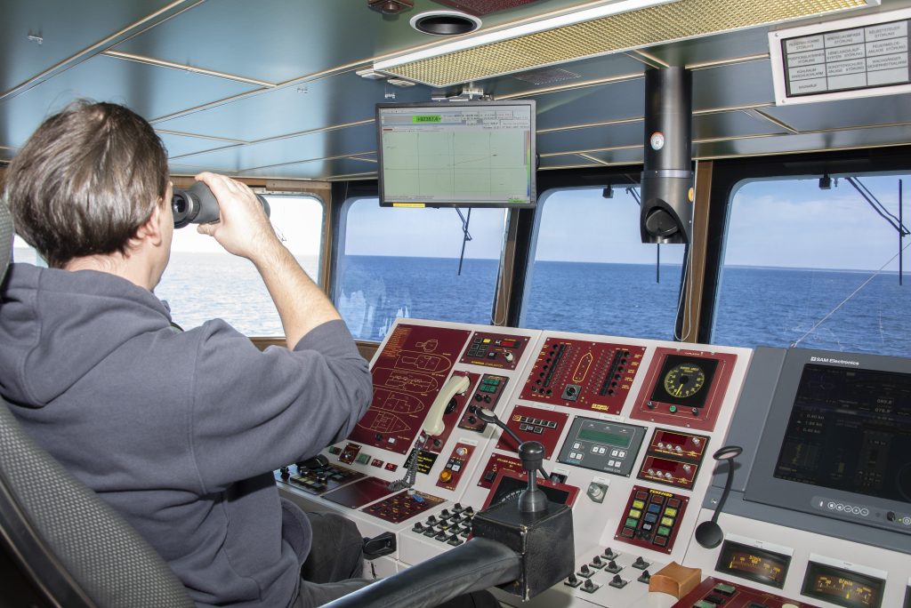 View from the bridge of the research vessel Deneb, with a crew member using binoculars and navigation equipment visible in the foreground.