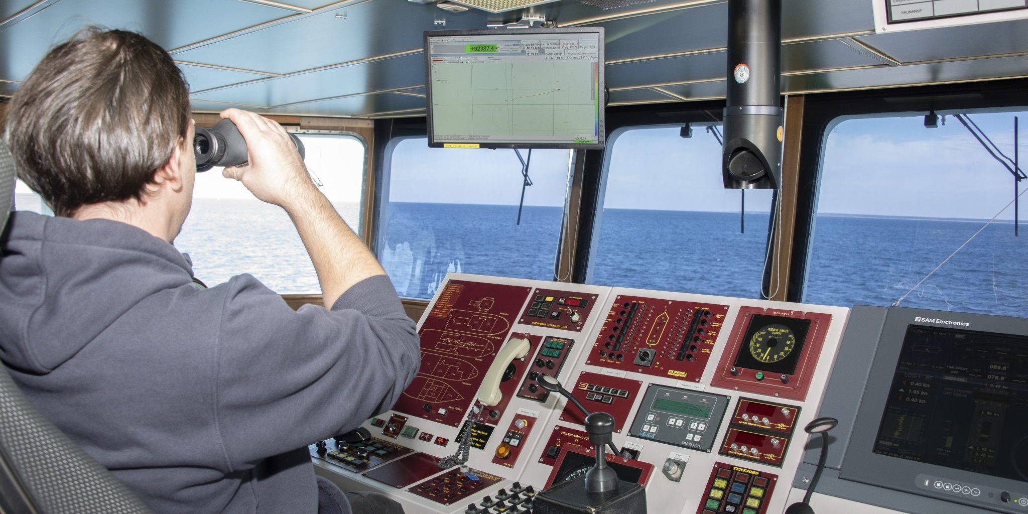 View from the bridge of the research vessel Deneb, with a crew member using binoculars and navigation equipment visible in the foreground.