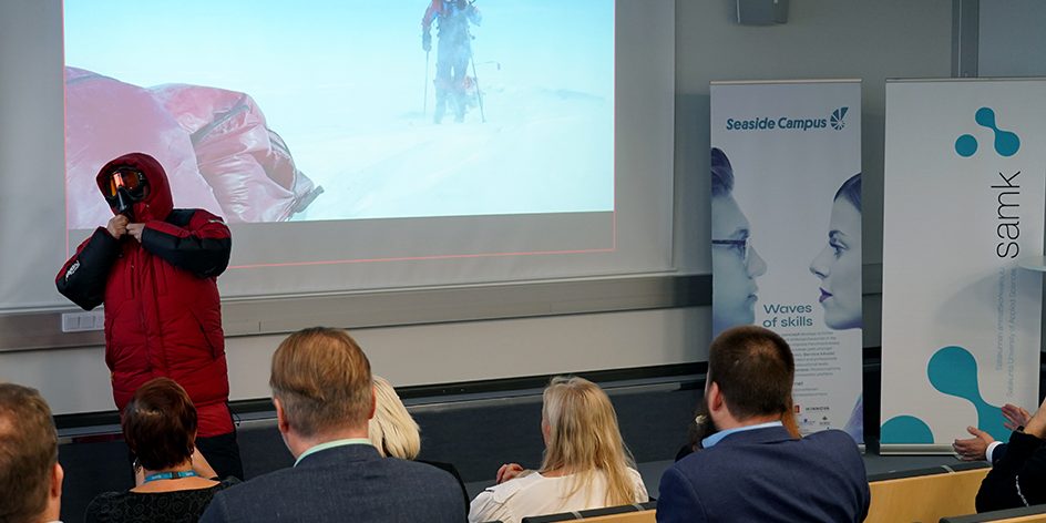 Poppis Suomela suurta talvitakkia päältään auditorion edessä.