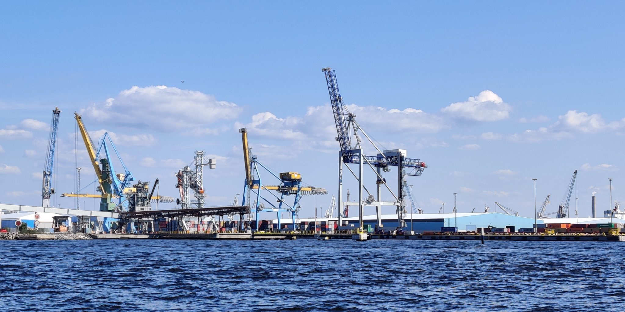 Harbor view with the sea in the foreground and cranes in the background.