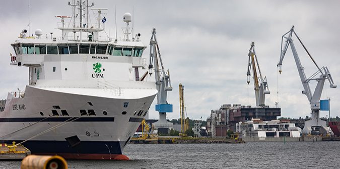 A cargo ship near the harbor. In the background, there are cranes.