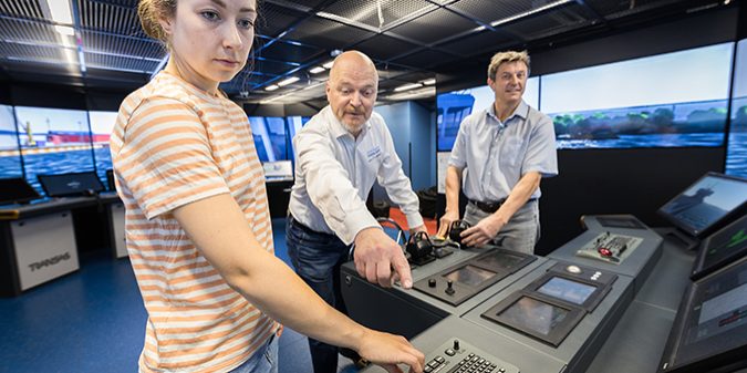 Three individuals are operating a maritime simulator.