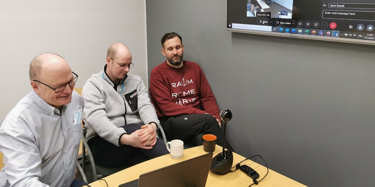 Three persons by a table, attending a meeting online.