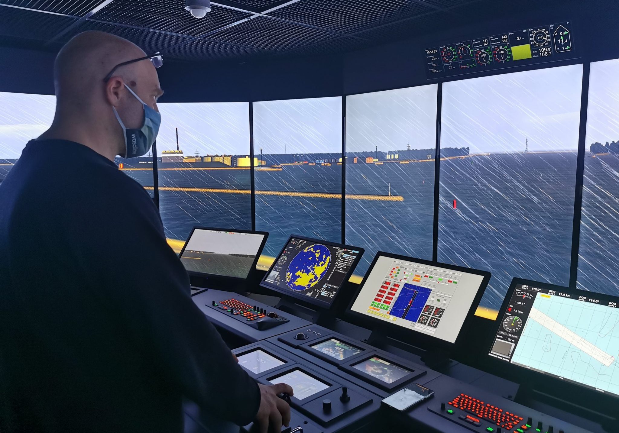 Yhteiskäyttösimulaattorit Kapteeni ohjaa laivaa merenkulun komentosiltasimulaattorissa. Näytöillä näkyy sateinen satamanäkymä.