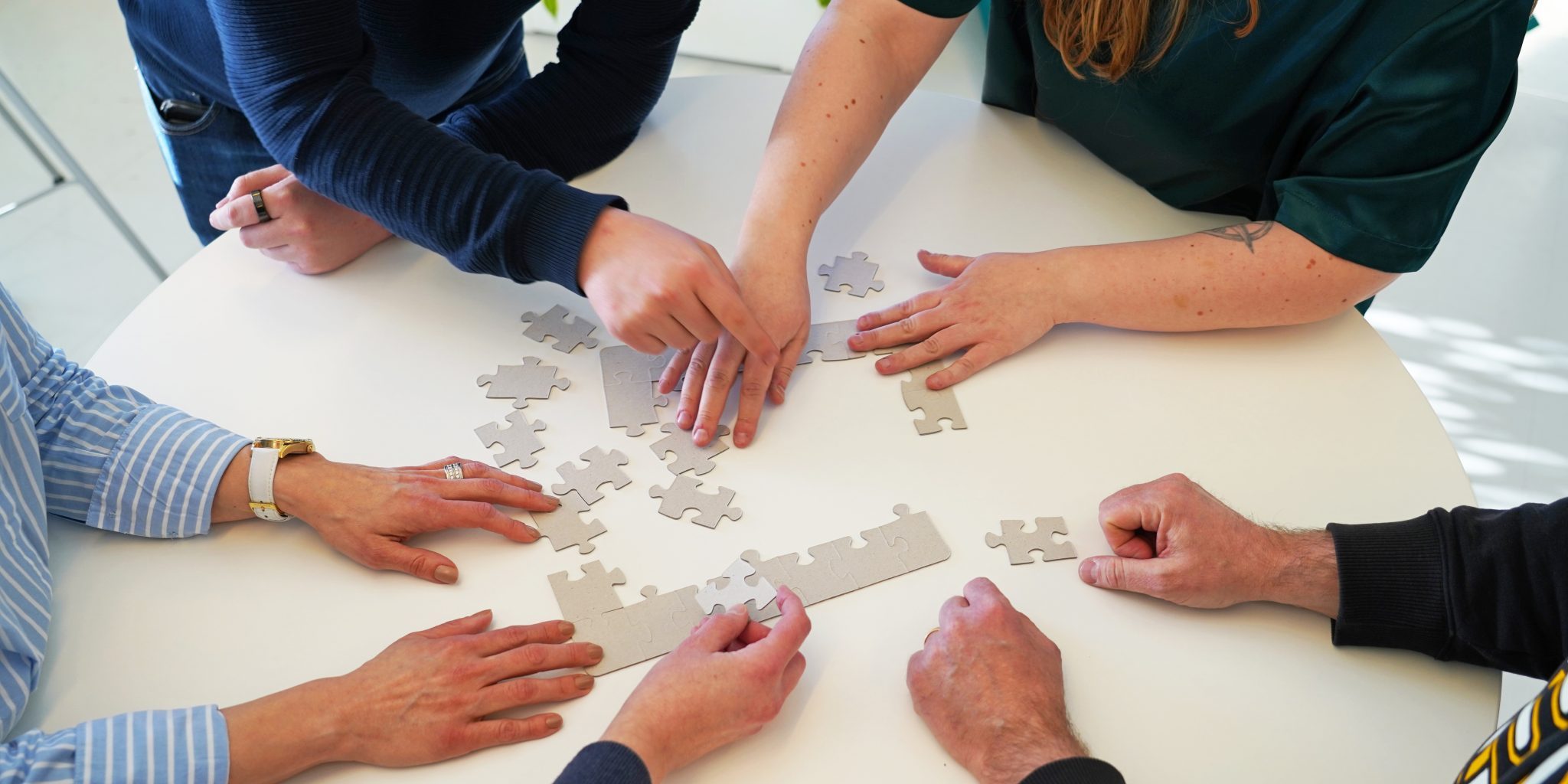 Hands on a table working with pieces of a puzzle together.